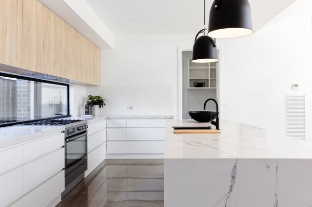 A white kitchen with a stone benchtop island and pendant light