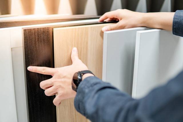 A hand pointing to laminate door samples in dark timber, light timber and soft grey finishes