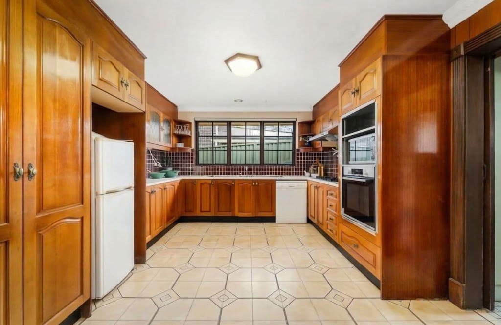 An older kitchen with orange timber cabinets and tiled floor, before its facelift