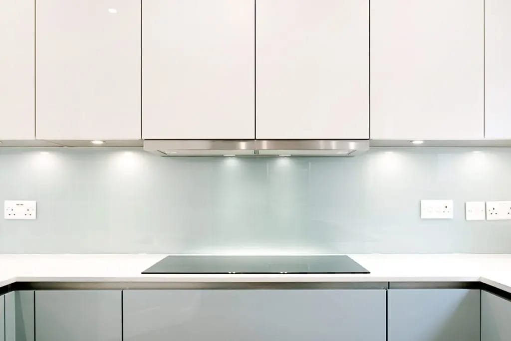 A glass splashback above a cooktop in a white kitchen